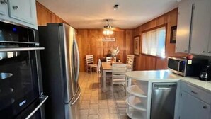 Una cucina moderna con forno a incasso, frigorifero e microonde. C'è un'area pranzo con tavolo e sedie, e un piccolo isolotto con lavello.