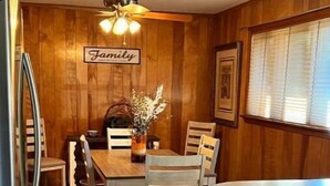 Un'area pranzo con rivestimenti in legno, un tavolo, sedie, una ventola a soffitto e un frigorifero.