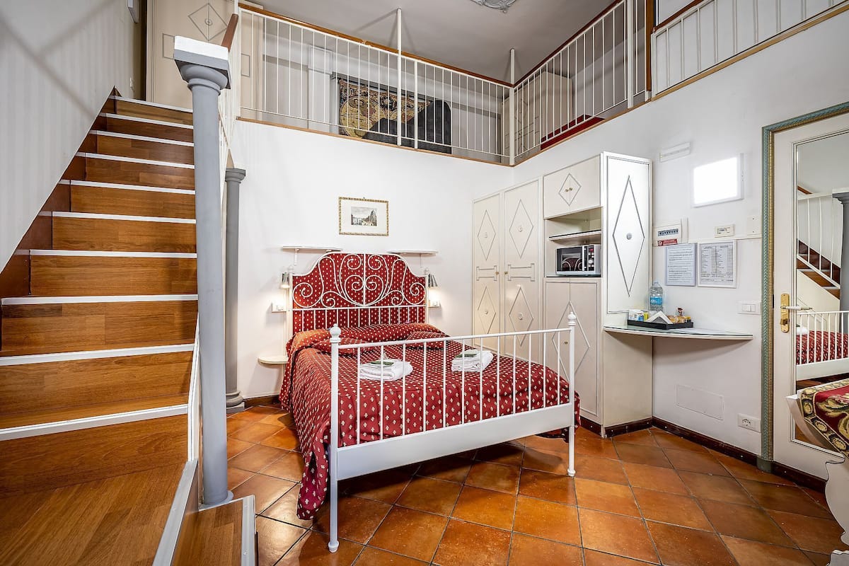 A bedroom with a bed, a chest of drawers, a desk, a mirror, and a staircase.