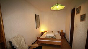 A small, cozy bedroom with a wooden bed, a chair, and a single wall-mounted light fixture.