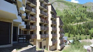 A multi-story hotel with balconies, set against a mountainous backdrop. - At the foot of shops, 2nd floor, view panoramic, balcony, tv, ski locker, 55m², Auris en Oisans (Auris)