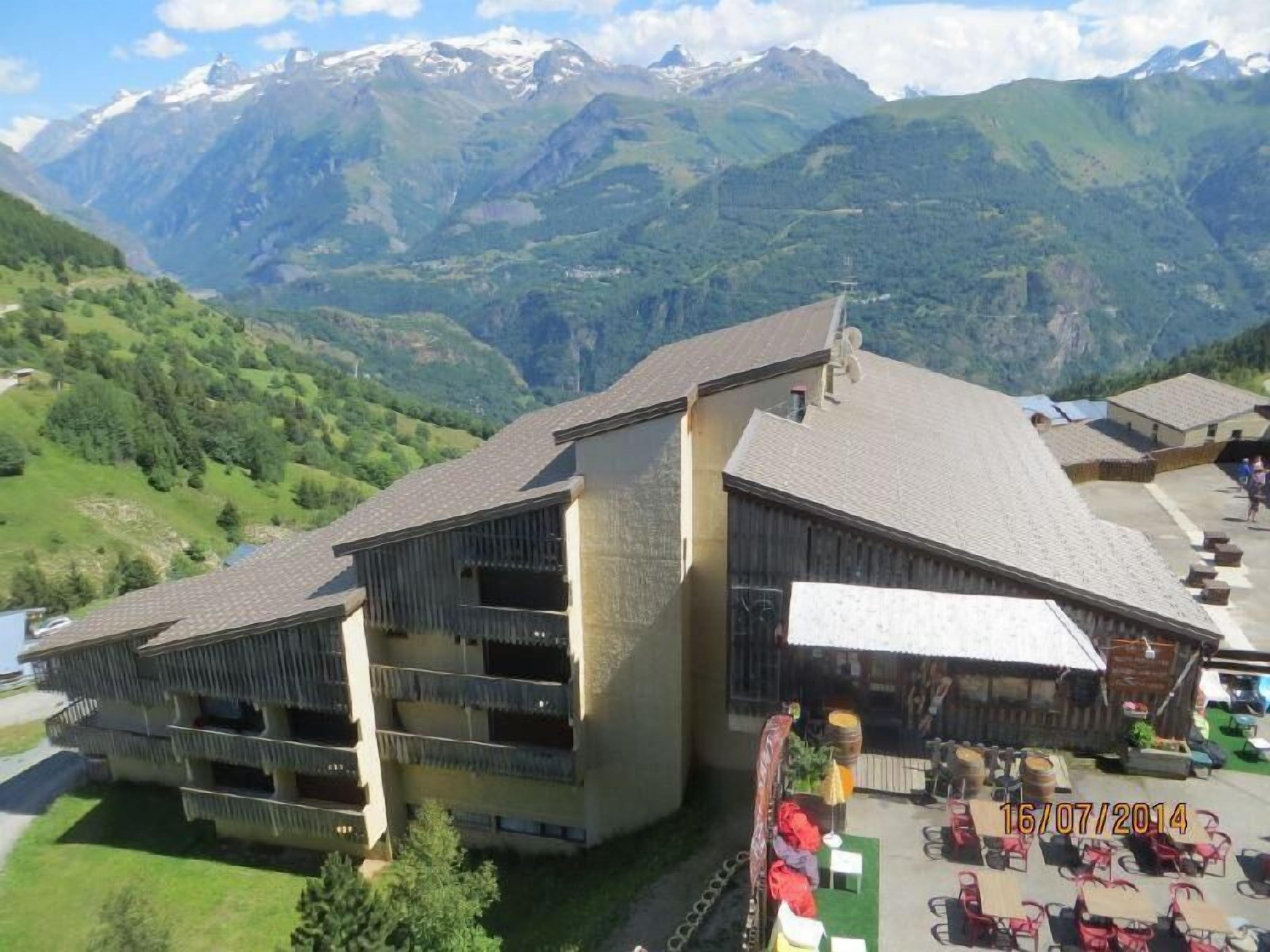 A building with a sloped roof, multiple balconies, and a patio area with outdoor seating.