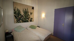A small, simple room with two beds, a wall-mounted painting, a door, and a nightstand with a lamp. - At the foot of shops, 2nd floor, view panoramic, balcony, tv, ski locker, 55m², Auris en Oisans (Auris)