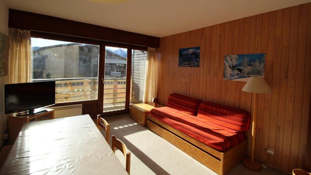 A room with a bed, a TV, a table, and a window with a view of buildings. - Ski-in/ski-out & foot of the slopes, Ground floor, view panoramic, balcony, tv, 40m² (Auris)