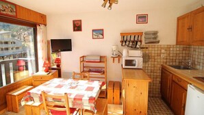 A compact kitchen with wooden cabinets, a microwave, a sink, and a table set for dining. - Ski-in/ski-out & foot of the slopes, 2nd floor, balcony, tv, 23m², Auris en Oisans (Auris)