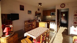 A compact kitchen with wooden cabinets, a microwave, and a dining table with a patterned tablecloth. - Ski-in/ski-out & foot of the slopes, 2nd floor, balcony, tv, 23m², Auris en Oisans (Auris)