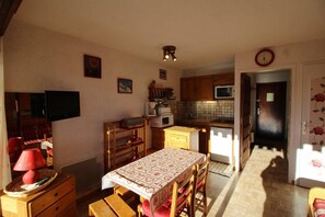 A compact kitchen with wooden cabinets, a microwave, and a dining table with a patterned tablecloth.