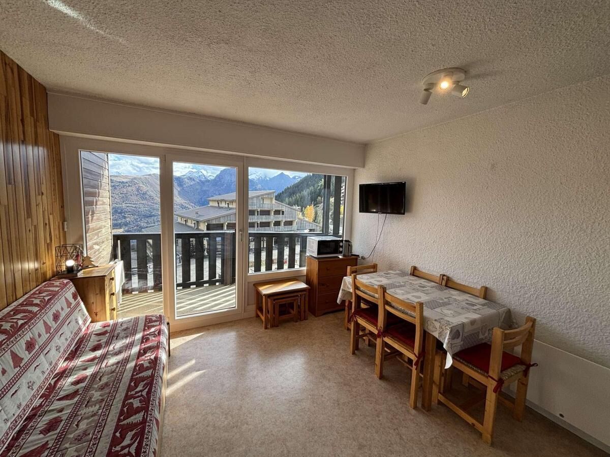 A bedroom with a bed, a wooden table with chairs, a TV, and a balcony with a mountain view.
