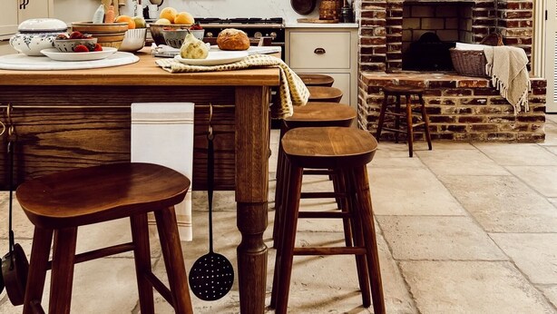 Une cuisine avec une cheminée en briques, des tabourets en bois et des ustensiles de cuisine suspendus.