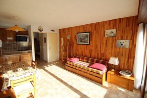 A cozy living room with a sofa, a dining table, and a kitchen area with wooden walls and a tiled backsplash.