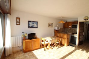 A compact kitchen with wooden cabinets, a dining table, and a TV.