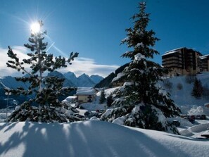 Un paisaje montañoso nevado, con un edificio y árboles en primer plano.