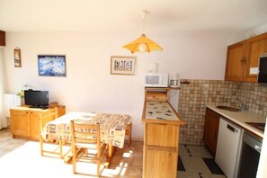 Una cocina compacta con armarios de madera, salpicadero de azulejos, microondas, lavamanos y un pequeño comedor con mesa y sillas.