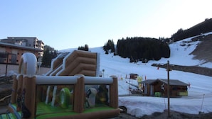 Eine aufblasbare Spielkonstruktion in einer verschneiten Außenlandschaft mit einer Skipiste und Gebäuden im Hintergrund.
