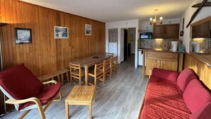 Ein gemütlicher Wohnbereich mit Esstisch aus Holz, einem roten Sofa und einer Küchenzeile.