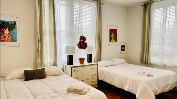 Habitación de hotel con dos camas, una mesita de noche con un jarrón de flores y cuadros en las paredes.