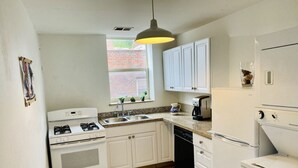 Una cocina compacta con armarios blancos, estufa, lavavajillas y refrigerador.