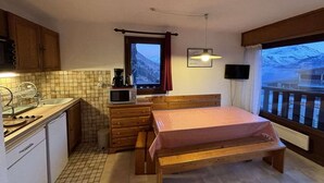 A compact bedroom with a wooden bed, a small kitchenette, a television, and a window with a view of a snowy mountain. - Ski-in/ski-out & foot of the slopes, 2nd floor, view panoramic, balcony, tv, 40m², Auris en Oisans (Auris)