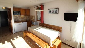A compact room with a bed, a small kitchenette, a television, and a window with curtains. - Ski-in/ski-out & foot of the slopes, 2nd floor, view panoramic, balcony, tv, 40m², Auris en Oisans (Auris)