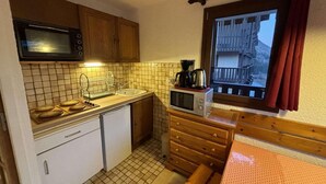 A compact kitchen with a microwave, stove, sink, and a small window with curtains. - Ski-in/ski-out & foot of the slopes, 2nd floor, view panoramic, balcony, tv, 40m², Auris en Oisans (Auris)