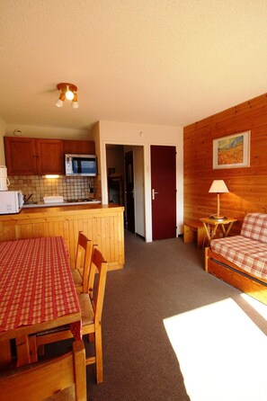 Quarto compacto com cozinha compacta, área de refeições com mesa e cadeiras, sofá e luminária.