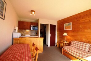 Un espacio habitable compacto con kitchenette, una zona de comedor con mesa y sillas, y un sofá.