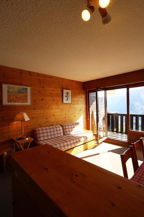 Relax in this inviting room with a plaid sofa, wooden table, and large window opening to a balcony with outdoor views.