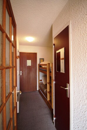A narrow hallway with a wooden door at the end, a bunk bed with a mirror, and a carpeted floor.