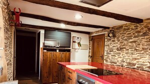 Une cuisine avec des meubles de rangement en bois, un plan de travail rouge, un four encastré et un mur en pierre.