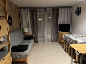 A compact living space with a sofa, a small table, a TV, and a bed.