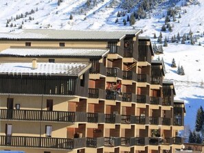 A multi-story hotel with balconies, a ski slope in the background, and a snowy landscape.