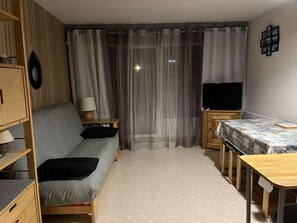 A compact living space with a sofa, a small table, a TV, and a bed.
