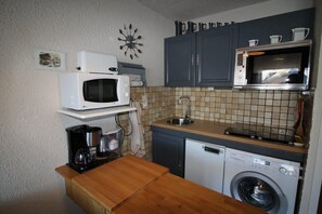 A compact kitchen with a microwave, oven, sink, and washing machine.