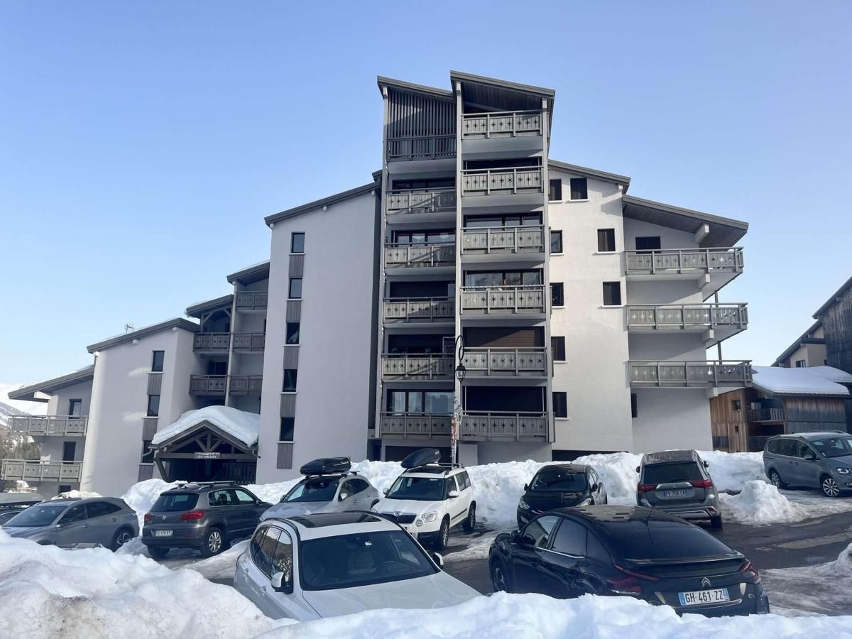 Um edifício de vários andares com varandas, um estacionamento com vários carros e neve no chão.