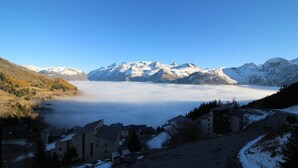 Un paysage montagneux aux sommets enneigés, un village avec des bâtiments et une vallée enveloppée de brume.