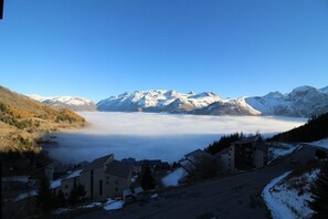 A mountainous landscape with snow-capped peaks, a village with buildings, and a valley shrouded in mist.