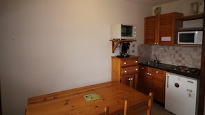A compact kitchen with wooden cabinets, a small refrigerator, a microwave, and a coffee maker on a shelf. - View mountain, balcony, parking, tv, ski locker, 23m², Auris en Oisans (Auris)