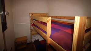 A small, compact room with two bunk beds, a wooden nightstand, and a small drawer unit.