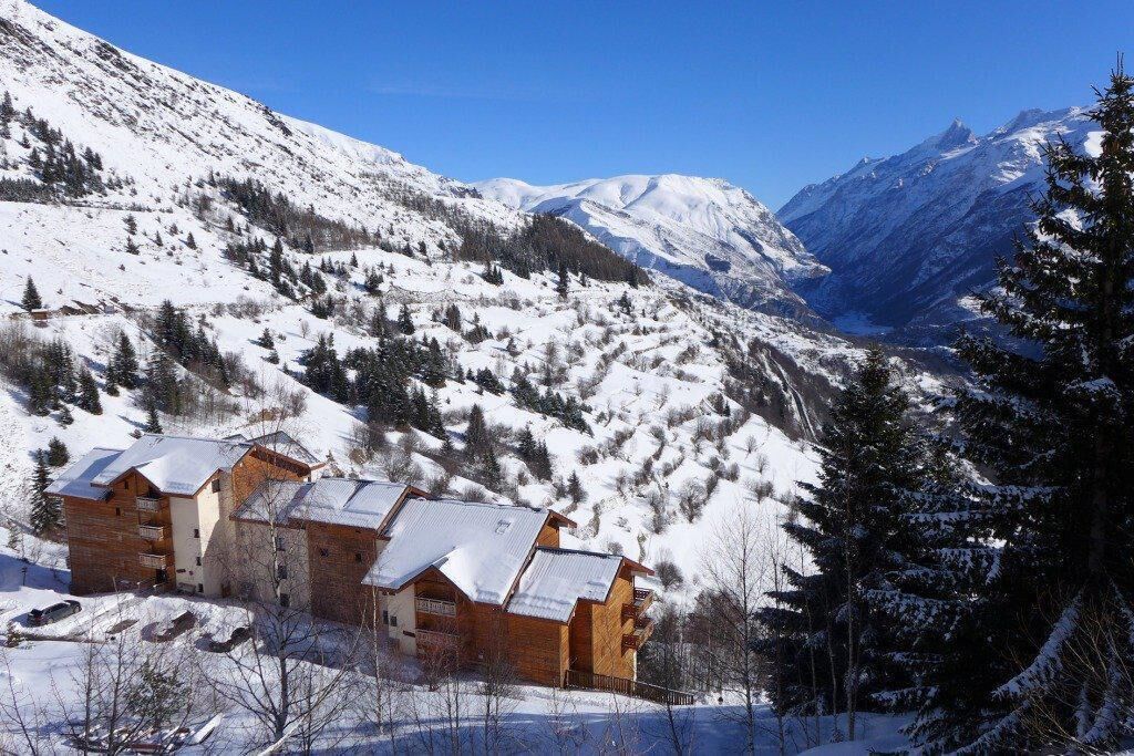 Ein Chalet-Stil-Gebäude mit mehreren Balkonen, umgeben von schneebedeckten Bergen und Bäumen.