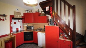 Une cuisine compacte avec des meubles rouges, un four à micro-ondes, un lave-vaisselle et un escalier en bois.