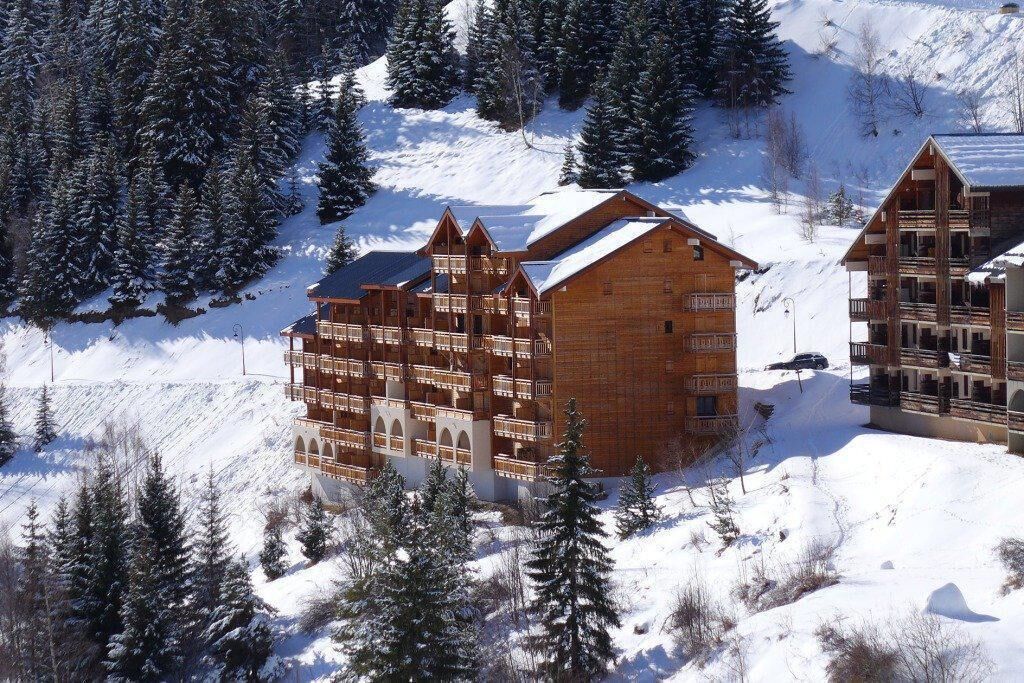 Een houten hotel in chalethuis-stijl met meerdere balkons, omgeven door sneeuwbedekte bomen en een bergachtig landschap.