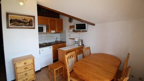 A compact kitchen with wooden cabinets, a microwave, a coffee maker, and a dining table with chairs.
