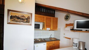 A compact kitchen with wooden cabinets, a microwave, a sink, a coffee maker, and a television.