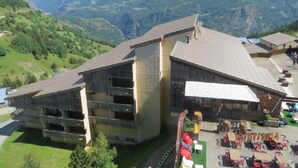 A building with a sloped roof, multiple balconies, and a patio area with outdoor seating.