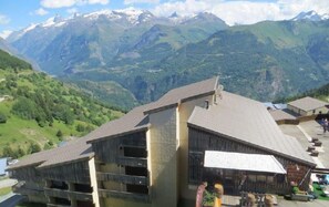 Un bâtiment doté d’un toit en pente, de plusieurs balcons et d’un patio aménagé avec des sièges extérieurs.