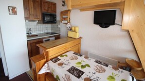 A compact kitchen with wooden cabinets, a microwave, a sink, and a small table with a tablecloth.