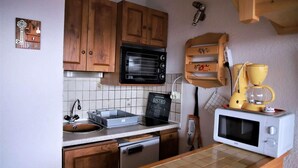 A compact kitchen with wooden cabinets, a black microwave, a white microwave, a coffee maker, and a sign that says "BISTRO".