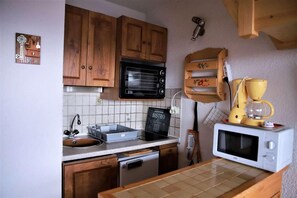 A compact kitchen with wooden cabinets, a black microwave, a white microwave, a coffee maker, and a sign that says "BISTRO".
