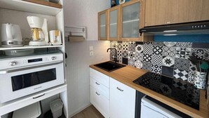 Una cocina compacta con armarios blancos, una estufa negra y azulejos decorativos en la pared.
