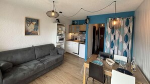Un espacio habitable compacto con sofá, mesa de comedor, zona de cocina y cortina estampada.